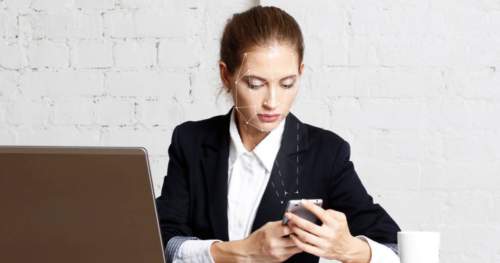 Una mujer en su oficina utiliza su teléfono móvil con una rejilla de reconocimiento facial sobre su rostro