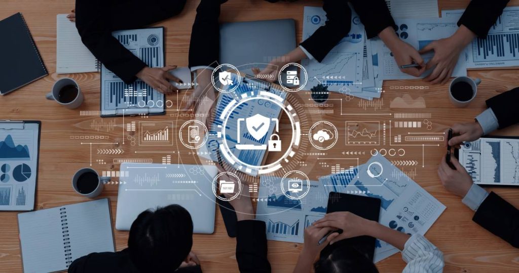 Vista cenital de un equipo de trabajo reunido alrededor de una mesa con gráficos digitales de seguridad informática superpuestos