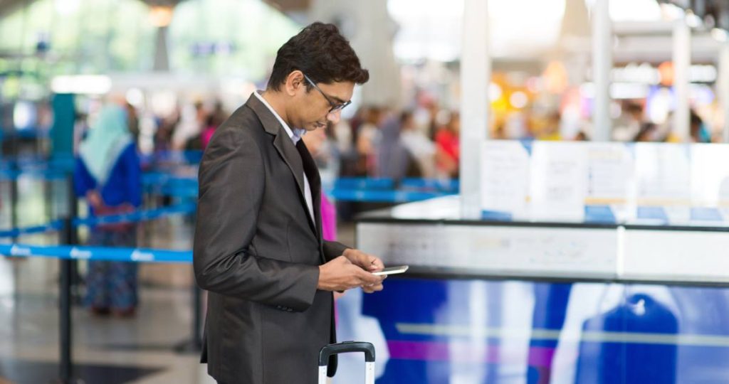 Un hombre con traje y maleta utilizando su teléfono móvil en la terminal de un aeropuerto