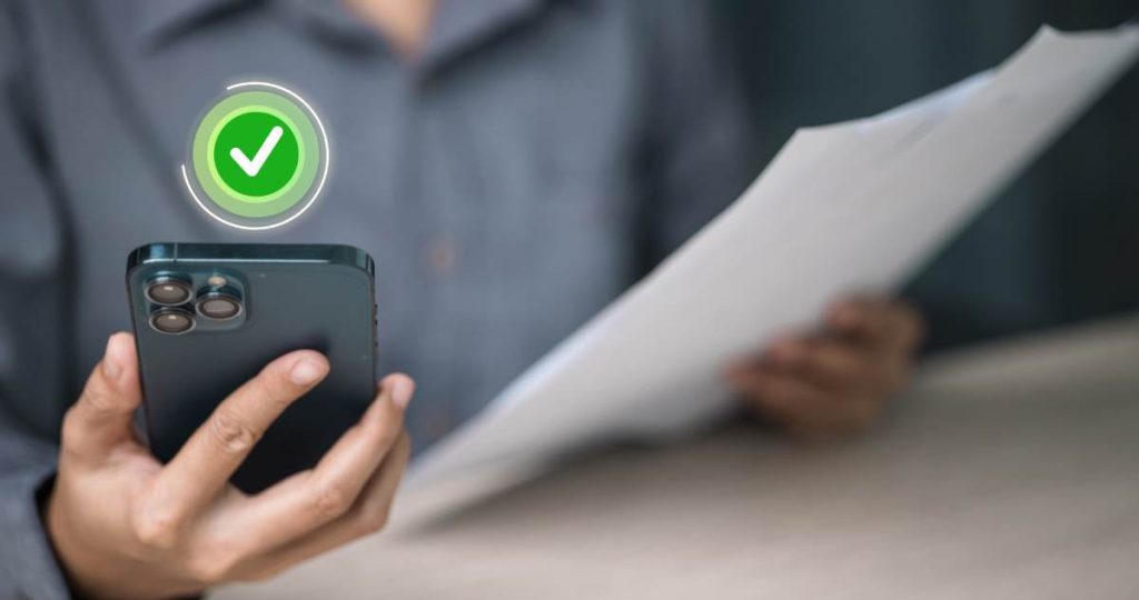 Una persona sostiene un teléfono móvil con un icono verde de verificación aprobada mientras sujeta un documento