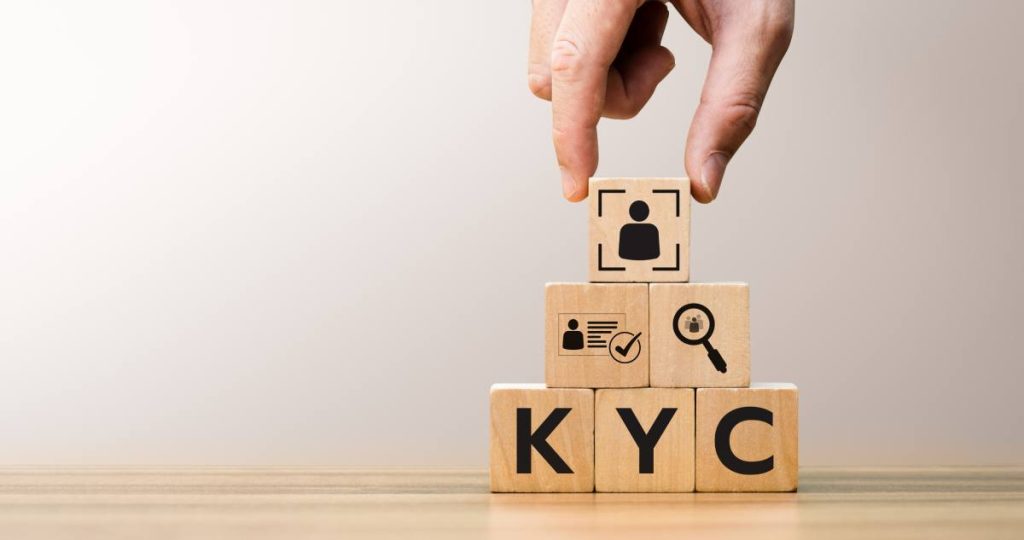 Una mano colocando un bloque con un icono de identidad sobre bloques de madera que forman las siglas KYC
