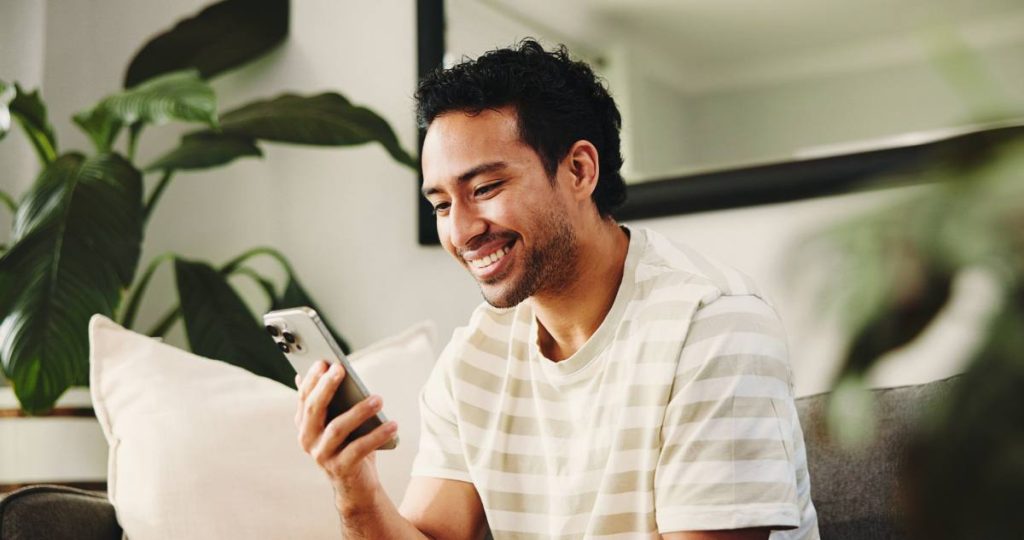 Un hombre sonriendo mientras usa un teléfono inteligente para un escaneo biométrico multimodal