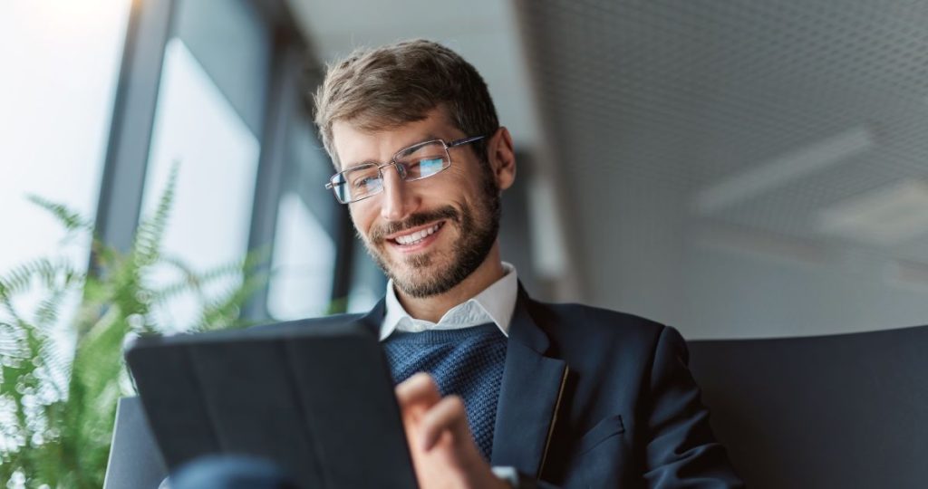 Un hombre sonriente con gafas y traje utiliza una tableta digital para realizar trámites online de forma eficiente