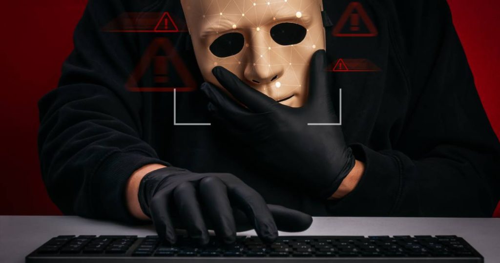 Una persona con guantes y máscara de reconocimiento facial teclea en un ordenador bajo alertas de seguridad