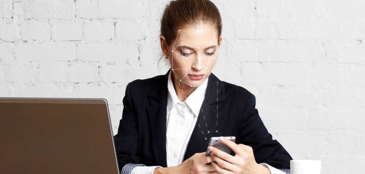 Una mujer en su oficina utiliza su teléfono móvil con una rejilla de reconocimiento facial sobre su rostro
