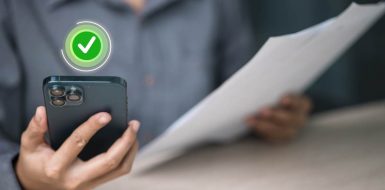 Una persona sostiene un teléfono móvil con un icono verde de verificación aprobada mientras sujeta un documento