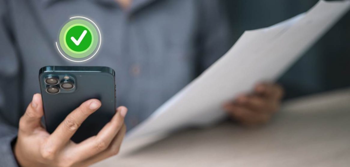 Una persona sostiene un teléfono móvil con un icono verde de verificación aprobada mientras sujeta un documento