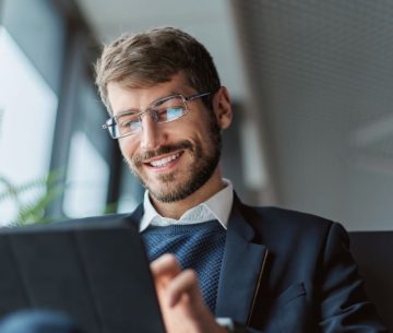 Un hombre sonriente con gafas y traje utiliza una tableta digital para realizar trámites online de forma eficiente