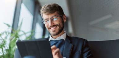 Un hombre sonriente con gafas y traje utiliza una tableta digital para realizar trámites online de forma eficiente