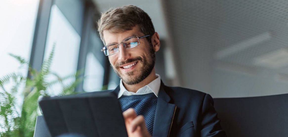 Un hombre sonriente con gafas y traje utiliza una tableta digital para realizar trámites online de forma eficiente