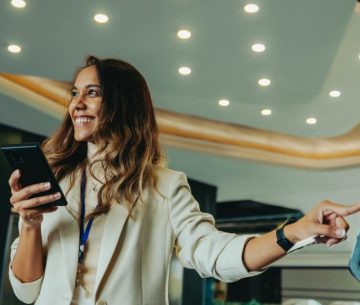 Una mujer sonriente sostiene su móvil mientras interactúa con una pantalla digital táctil