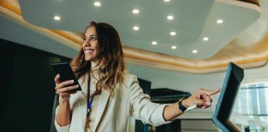 Una mujer sonriente sostiene su móvil mientras interactúa con una pantalla digital táctil