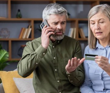 Una pareja mayor con gesto de preocupación mira una tarjeta de crédito mientras el hombre habla por teléfono