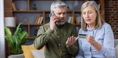 Una pareja mayor con gesto de preocupación mira una tarjeta de crédito mientras el hombre habla por teléfono